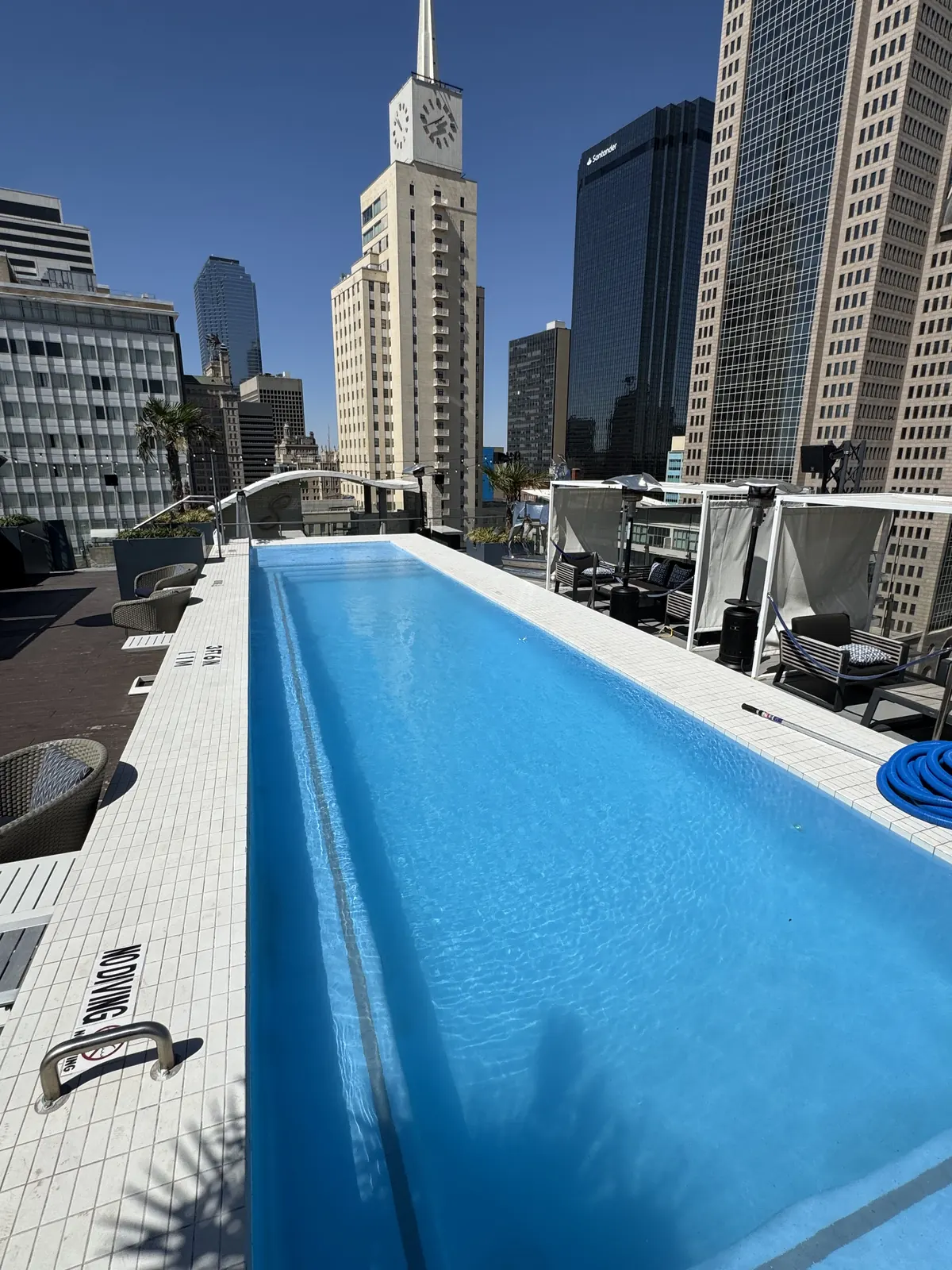 A rooftop lap pool on a downtown Dallas building, looking along the water towards the Mercantile clock tower and the city skyline