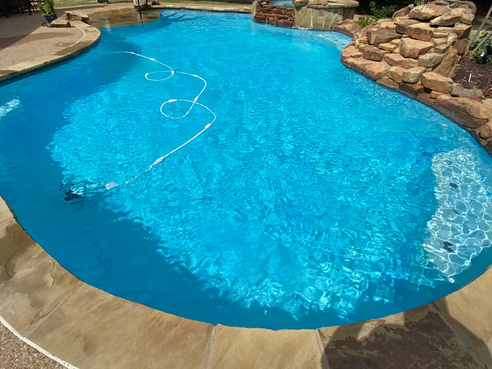 A freeform pool with a stacked stone waterfall and a raised spa along the far edge, at a home in Frisco, Texas