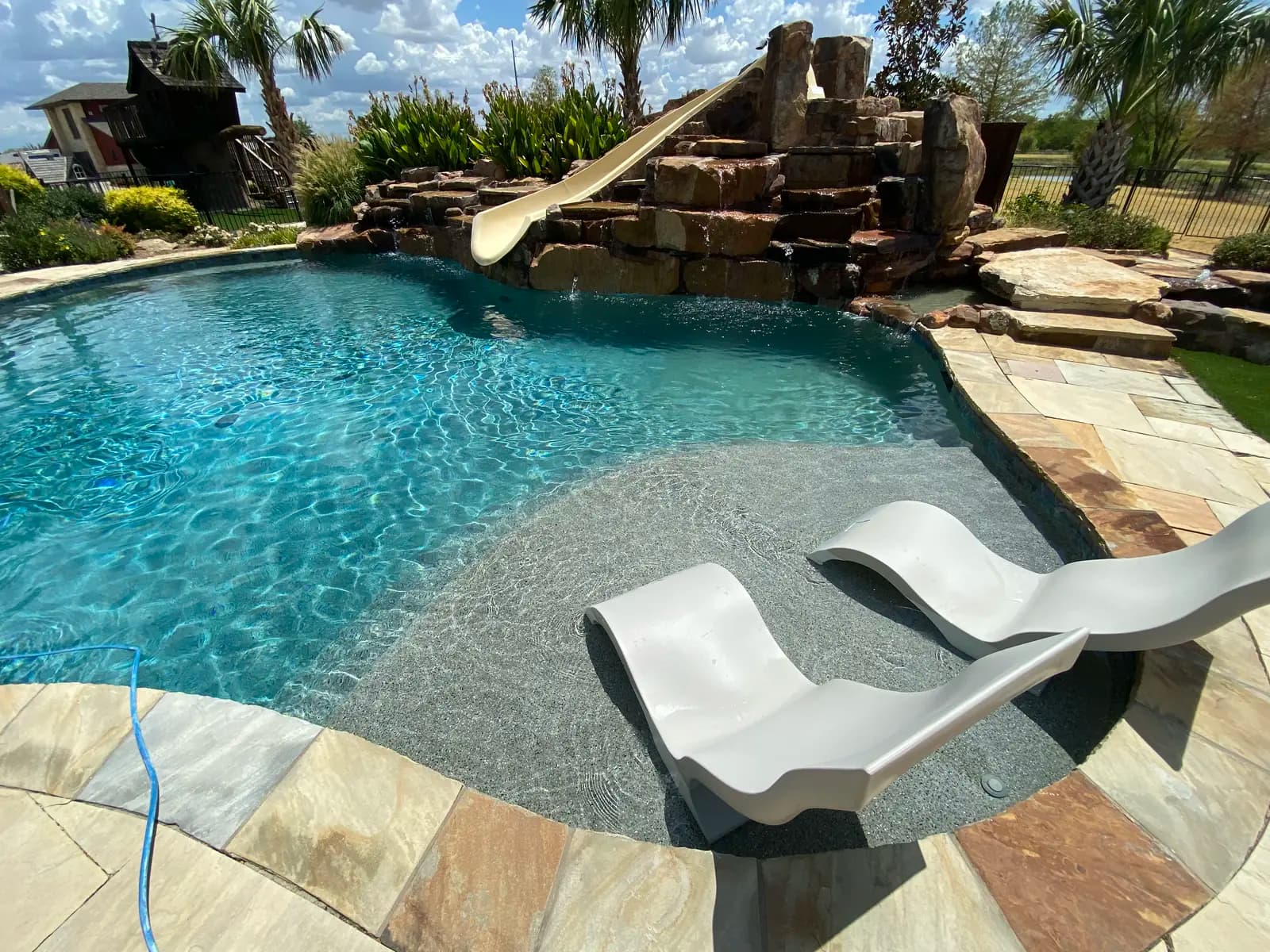 A freeform pool with a rock waterfall and slide, and two in-water loungers on a shallow tanning ledge, at a home in Lewisville, Texas