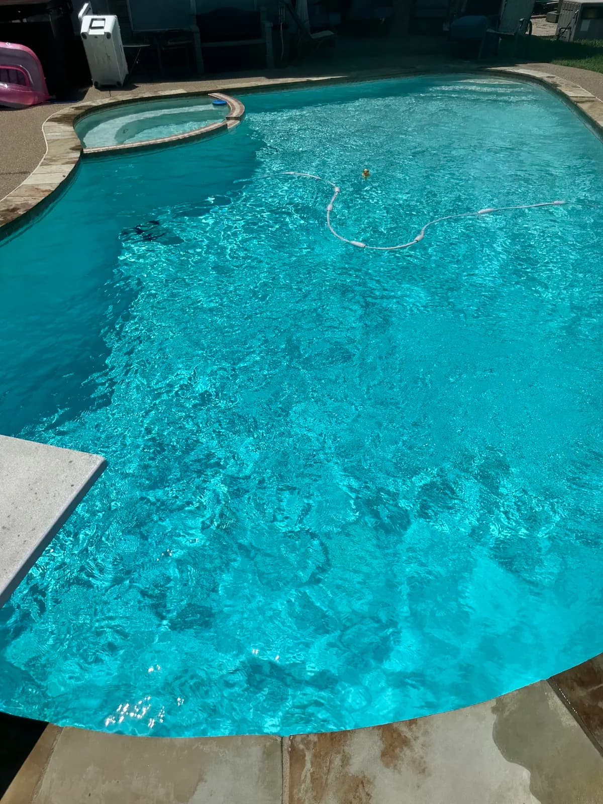 A freeform pool with an attached spa and a diving board, clear enough to read the floor, at a home in Murphy, Texas