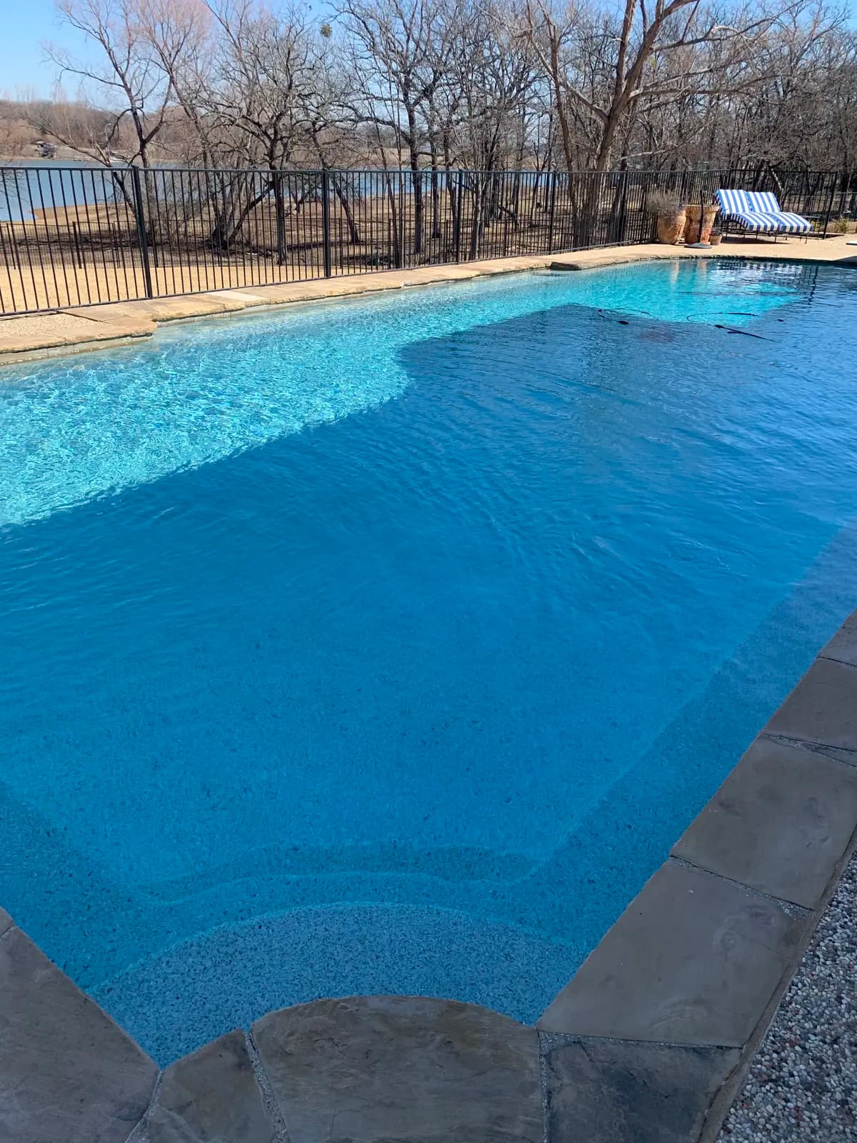 A large rectangular pool with flagstone coping, fenced off from a pond and bare winter trees on the land beyond, at a property in Parker, Texas