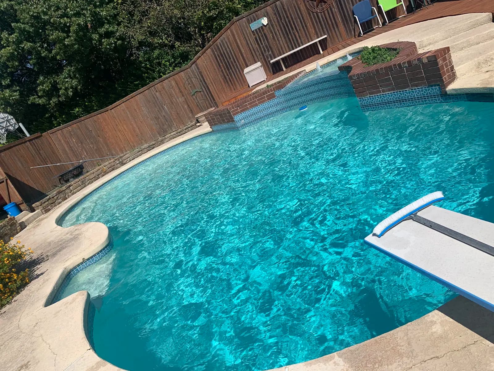 A freeform pool in Plano, Texas, with sheer descent spouts falling from a tiled raised wall and a diving board at the near corner