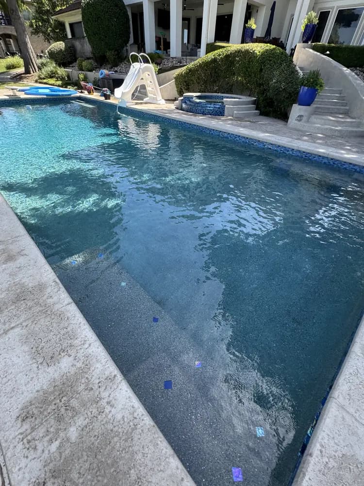 A lakefront pool looking back towards the house, with a raised spa, planters and stone steps beyond it