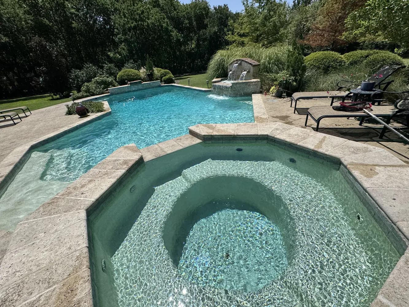 A raised octagonal spa spilling into a freeform pool, with travertine coping