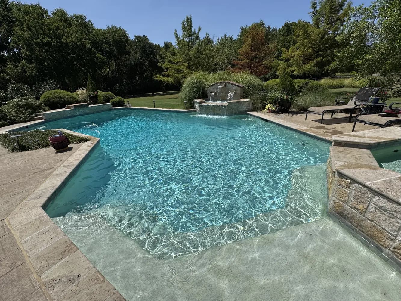 The tanning ledge of a freeform pool, with a cut-stone spillway behind it