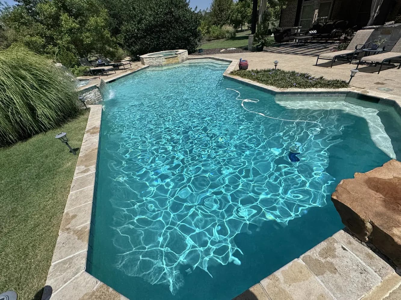 A freeform pool seen from the house, with a stone water feature beyond it
