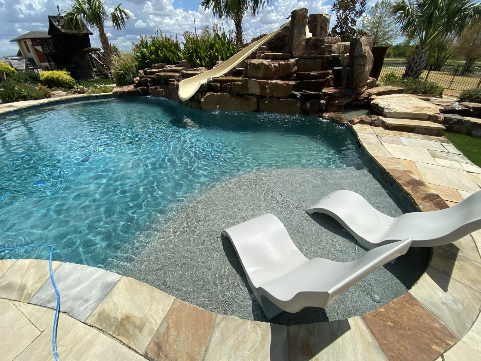 A freeform pool with a rock waterfall and slide, and two in-water loungers on a shallow tanning ledge, at a home in Lewisville, Texas